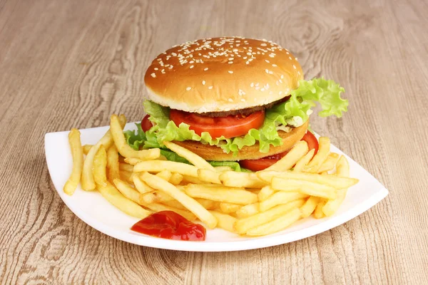 Grote en smakelijke hamburger en gebakken aardappelen op plaat op houten tafel — Stockfoto