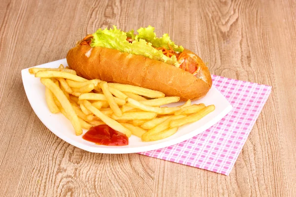 Cachorro quente apetitoso com batatas fritas na placa na mesa de madeira — Fotografia de Stock