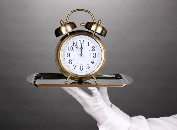 Hand i handske håller silverbricka med väckarklocka på grå bakgrund — Stockfoto