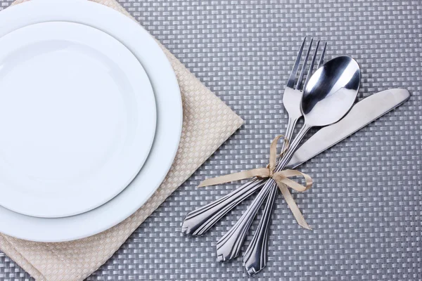 Белые пустые тарелки с вилкой, ложкой и ножом, завязанные лентой на серой скатерти — стоковое фото
