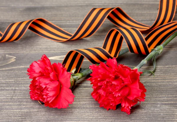 Carnations and St. George's ribbon on grey wooden background — Stock Photo, Image