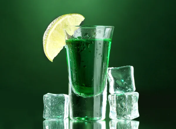 Glass of absinthe, lime and ice on green background — Stock Photo, Image
