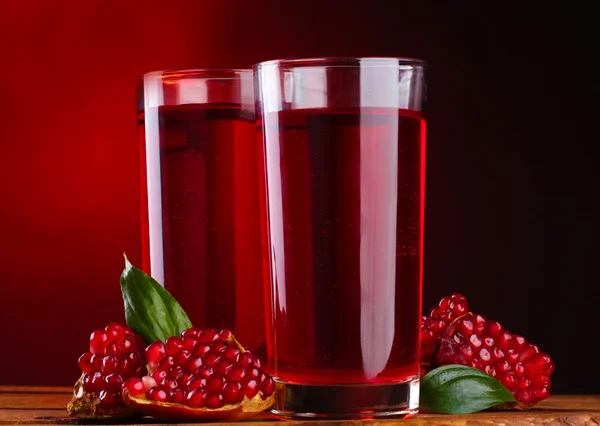 Pomergranato maturo e bicchieri di succo su tavolo di legno su sfondo rosso — Foto Stock