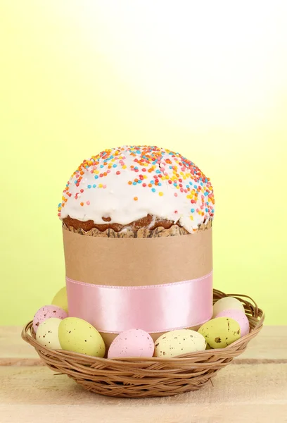 Krásné velikonoční dort v koši s vejce na dřevěný stůl na zeleném pozadí — Stock fotografie
