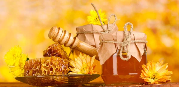 Zwei Gläser Honig, Waben und hölzerner Nieselregen auf dem Tisch auf gelbem Hintergrund — Stockfoto