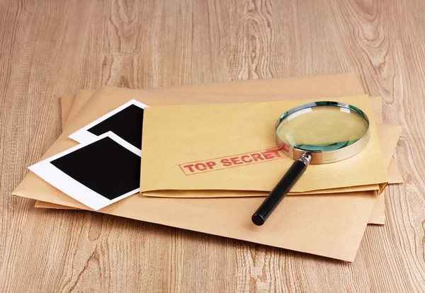 Enveloppen met top geheime stempel met fotopapier en vergrootglas op houten achtergrond — Stockfoto