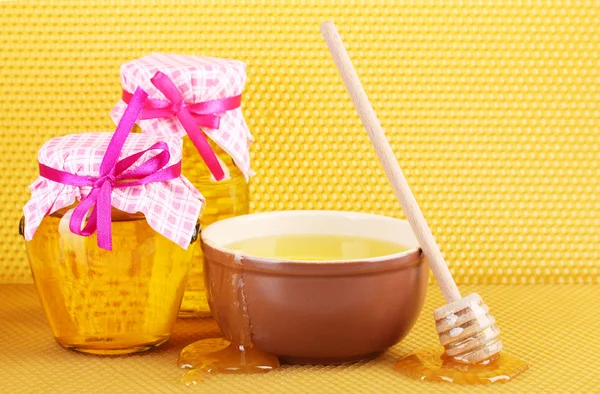 Frascos de miel, tazón y rociador de madera con miel sobre fondo de panal amarillo —  Fotos de Stock