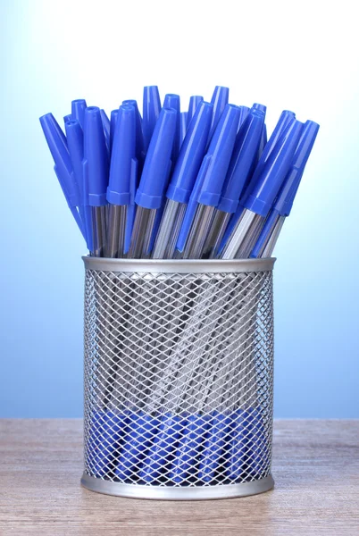 Голубые ручки в металлической чашке на деревянном столе на голубом фоне — стоковое фото
