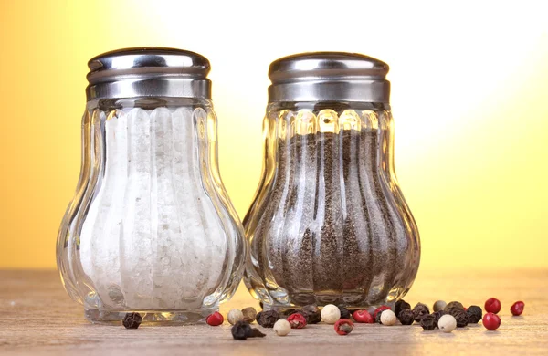 Salt and pepper mills on wooden table on yellow background — Stock Photo, Image