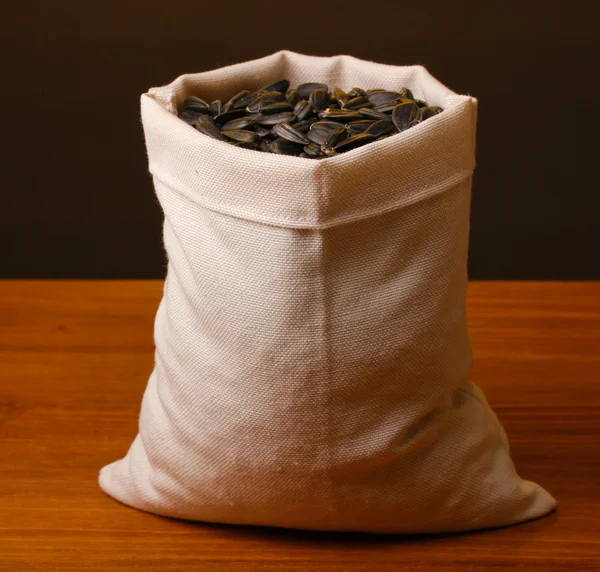 Cloth bag of sunflower seeds on wooden table on brown background — Stock Photo, Image