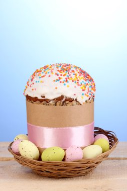 Beautiful Easter cake in basket with eggs on wooden table on blue background