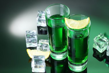 Two glasses of absinthe, lemon and ice on green background clipart