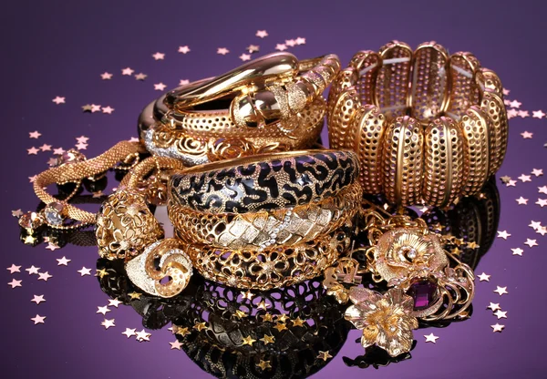 Beautiful golden jewelry on purple background — Stock Photo, Image