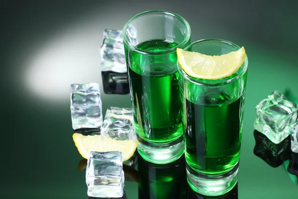 Two glasses of absinthe, lemon and ice on green background — Stock Photo, Image