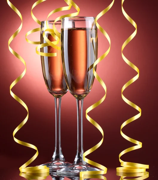 Glasses of champagne and streamer on red background — Stock Photo, Image