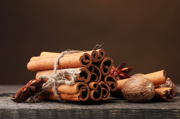 Cinnamon sticks, nutmeg and anise on wooden table on brown background