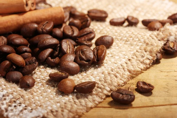 Grãos de café e paus de canela no saque na mesa de madeira — Fotografia de Stock