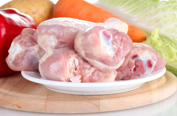 Fresh vegetables with raw chicken drumsticks on cutting board isolated on white — Stock Photo, Image