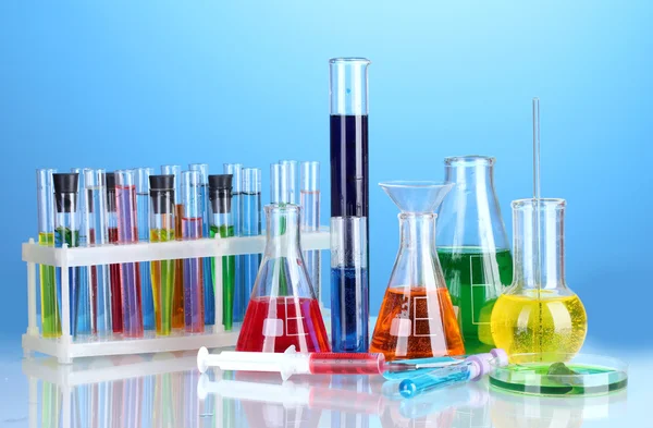 Different laboratory glassware with color liquid on blue background — Stock Photo, Image