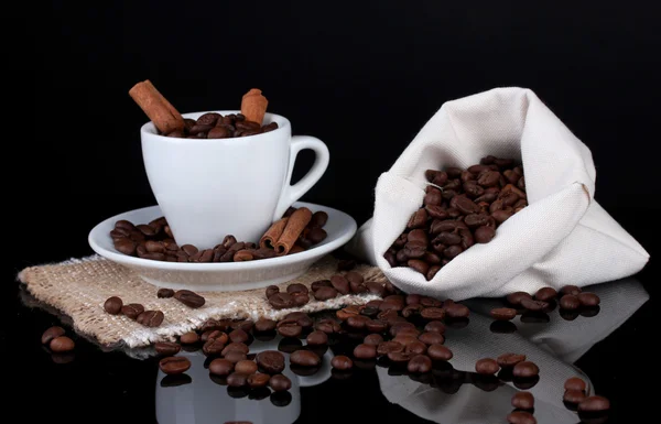 Composición del saco de lona y la taza con granos de café sobre fondo negro — Foto de Stock