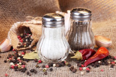 Salt and pepper mills and spices on burlap background clipart