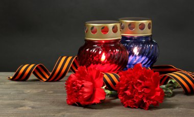 Memory lantern with candles, red carnations and St. George ribbon on wooden table on grey background clipart