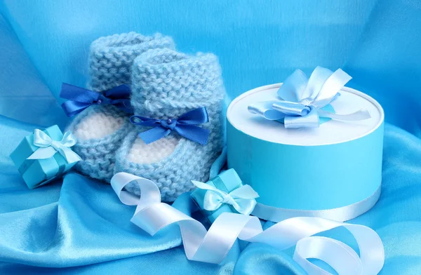 Schöne Geschenke und Babystiefel auf blauer Seide — Stockfoto