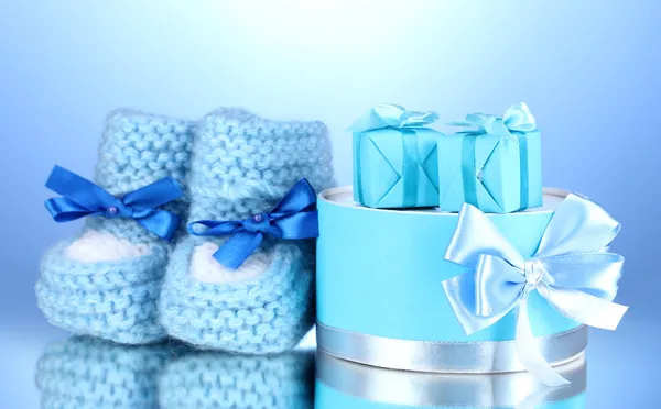 精美的礼物和在蓝色背景上的婴儿毛线鞋 — 图库照片