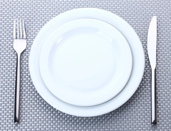Placas brancas vazias com garfo e faca em uma toalha de mesa cinza — Fotografia de Stock