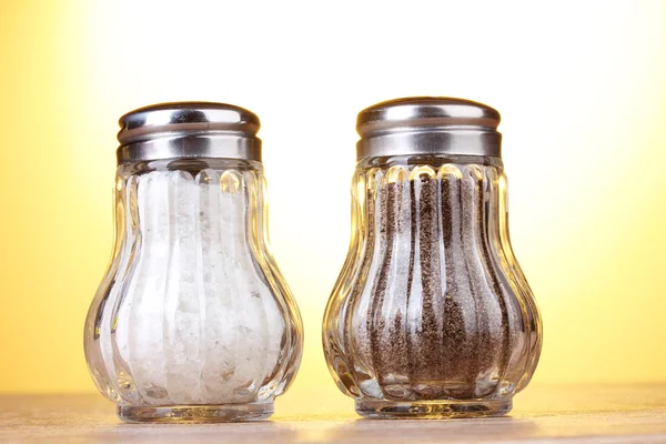 Salz- und Pfeffermühlen auf Holztisch auf gelbem Hintergrund — Stockfoto