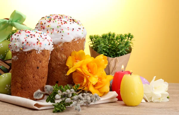 漂亮的复活节蛋糕、 丰富多彩的蛋和黄色背景上的木桌上的蜡烛 — 图库照片