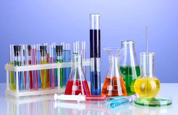 Vidros de laboratório diferentes com líquido de cor no fundo violeta — Fotografia de Stock
