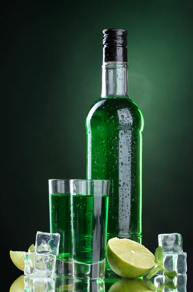 Bottle and glasses of absinthe with lime and ice on green background — Zdjęcie stockowe