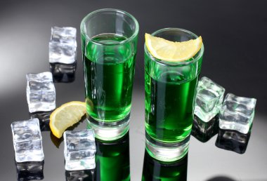 Two glasses of absinthe, lemon and ice on grey background clipart