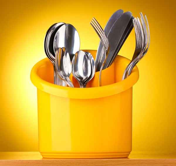 Keuken bestek, messen, vorken en lepels in geel staan op gele achtergrond — Stockfoto