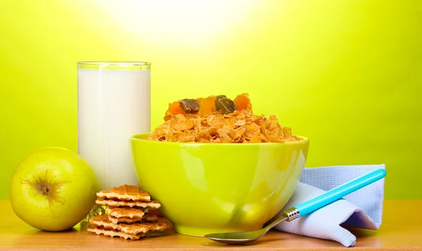 在绿色碗、 苹果和一杯牛奶在绿色背景上的木桌上的美味玉米片 — 图库照片