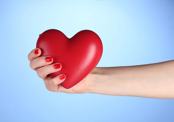Corazón rojo en la mano de la mujer sobre fondo azul — Foto de Stock