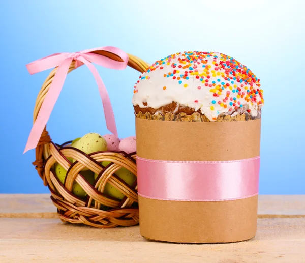 Beautiful Easter cake with eggs in basket on wooden table on blue background — Stock Photo, Image