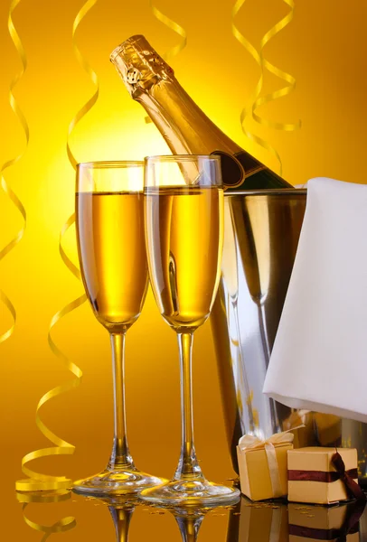 Üveg pezsgő vödörben jég és a pohár pezsgő, sárga háttér — Stock Fotó