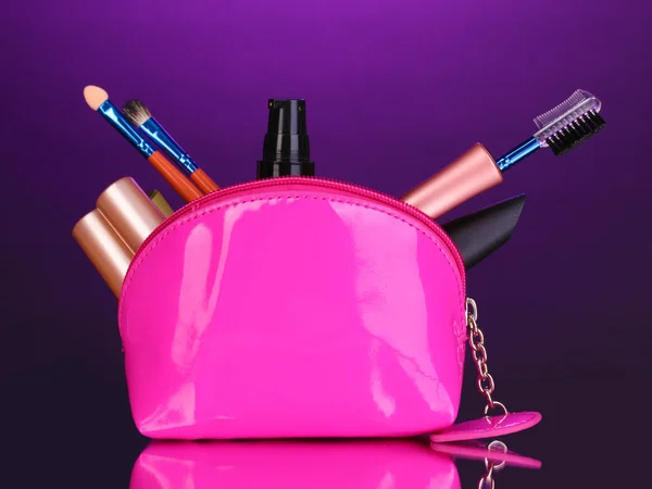 Make up bag with cosmetics and brushes on violet background — Stock Photo, Image