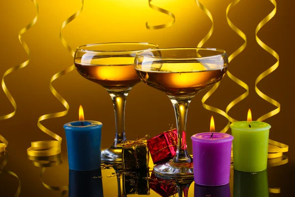 Glas champagne, ljus, gåvor och streamer på gul bakgrund — Stockfoto