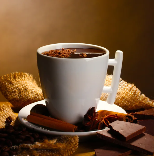 Taza de chocolate caliente, palitos de canela, nueces y chocolate en la mesa de madera sobre fondo marrón — Foto de Stock