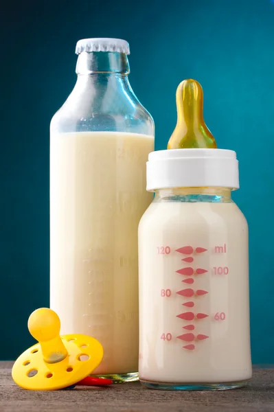 Flaskor av mjölk och nappen på träbord på blå bakgrund — Stockfoto