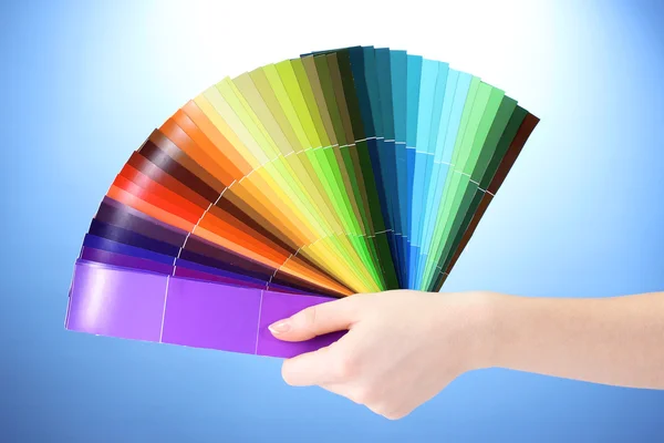 Hand som håller ljusa palett av färger på blå bakgrund — Stockfoto
