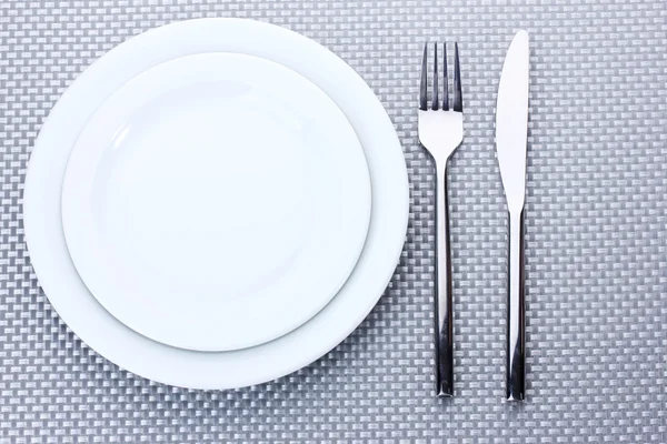 Белые пустые тарелки с вилкой и ножом на серой скатерти — стоковое фото