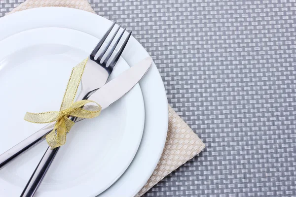 Білі порожні тарілки з виделкою і ножем пов'язані стрічкою на сірій скатертині — стокове фото