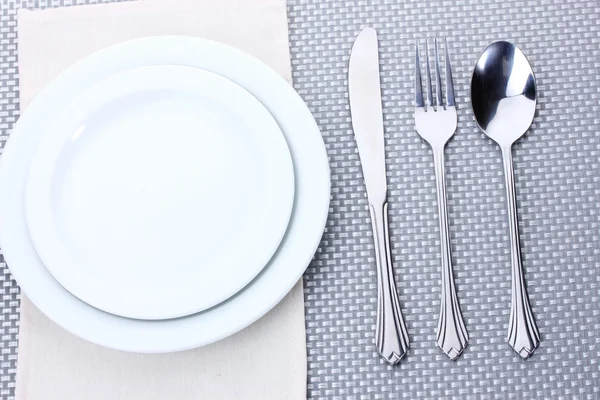 Piatti bianchi vuoti con forchetta, cucchiaio e coltello su una tovaglia grigia — Foto Stock