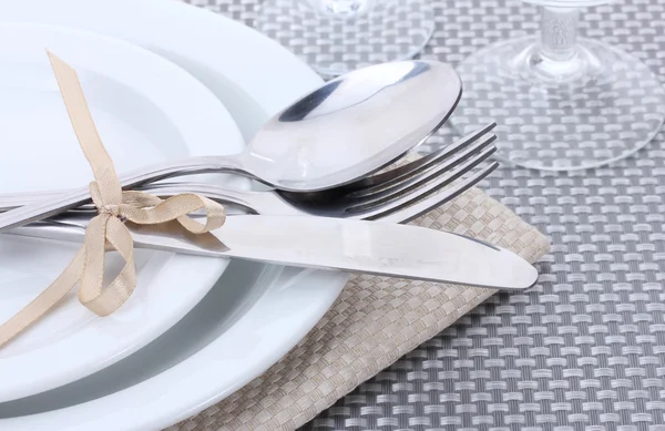 Белые пустые тарелки, вилка и нож, связанные лентой и стаканами на серой скатерти — стоковое фото