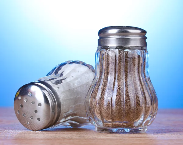 Sůl a pepř mlýny na dřevěný stůl na modrém pozadí — Stock fotografie