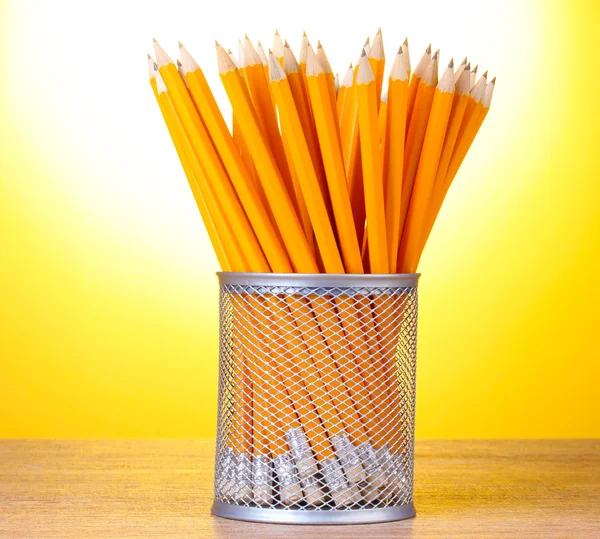 Ołówków w metalowy kubek na drewnianym stole na żółtym tle — Zdjęcie stockowe